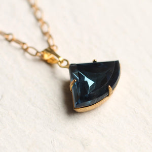 Overhead shot of the navy blue fan-shaped pendant on a gold-plated chain.