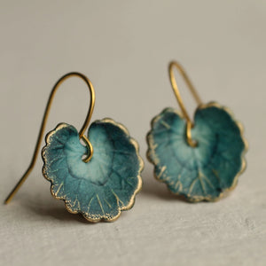 Side angle of navy blue and gold leaf earrings with scalloped edges, showing detailed veining and curved brass ear wires on a neutral background.