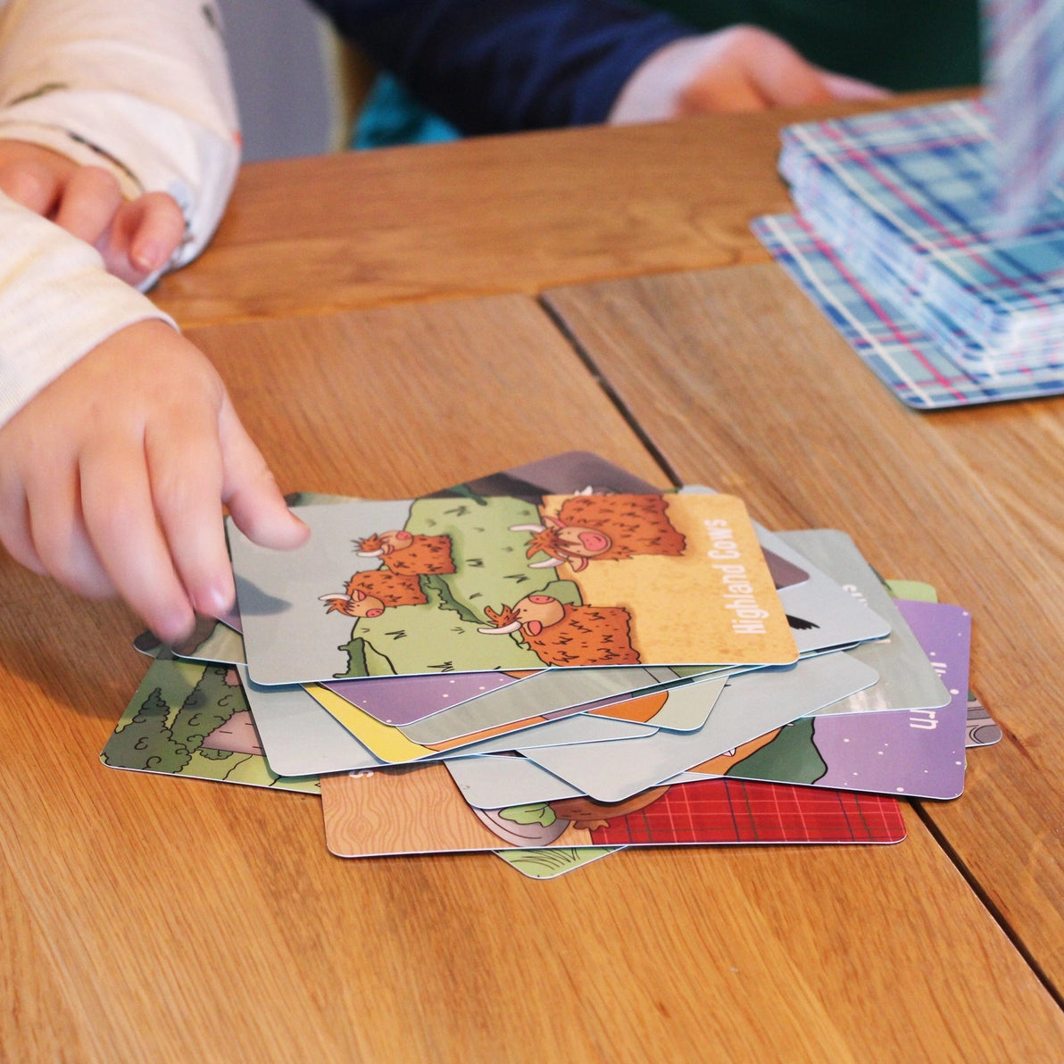 Two young children playing Scotland Snap card game at a wooden table.