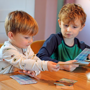 Two young children playing Scotland Snap card game at a wooden table.