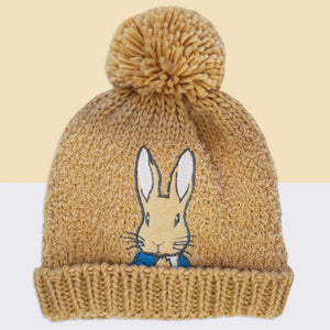Child wearing Peter Rabbit™ hat and gloves, hands covering face – cute neutral knit beanie set for kids.