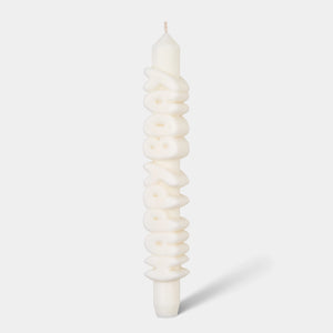 Studio image of a 9-inch white taper candle with bold, sculpted “HAPPY BDAY” lettering running vertically, handmade from eco-friendly wax blend.