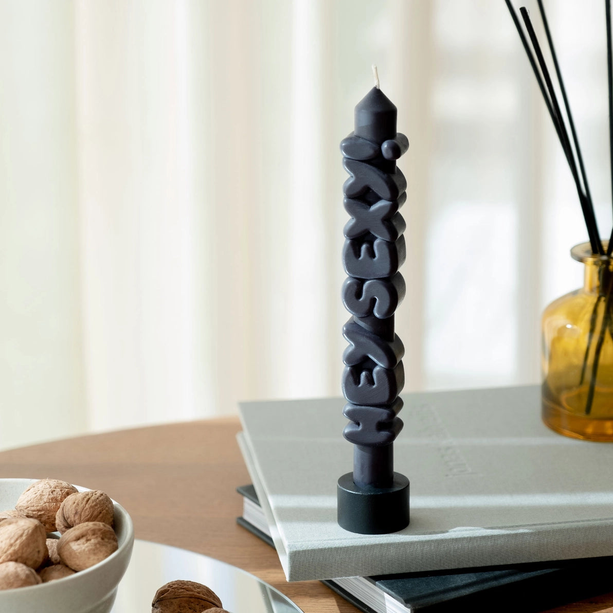 Black ‘Hey Sexy!’ taper candle standing upright on stacked books, styled with modern home decor and soft natural light.