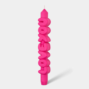Front view of a bright pink taper candle spelling out “LOVE YOU” in chunky 3D letters, standing upright against a light grey background.