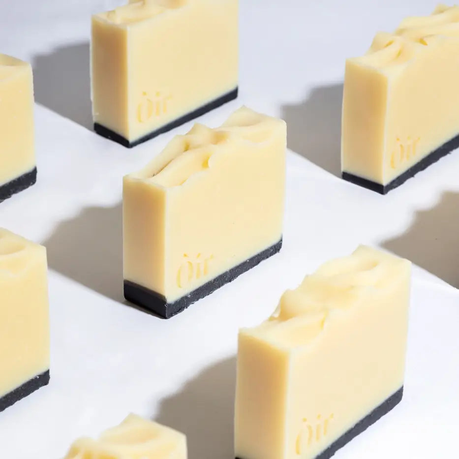 Multiple Òir Cinnamon & Lemongrass Soap bars arranged upright on white background, showing creamy tops and deep black charcoal base.