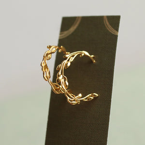 The olive branch gold hoop earrings displayed on an olive green linen presentation card.