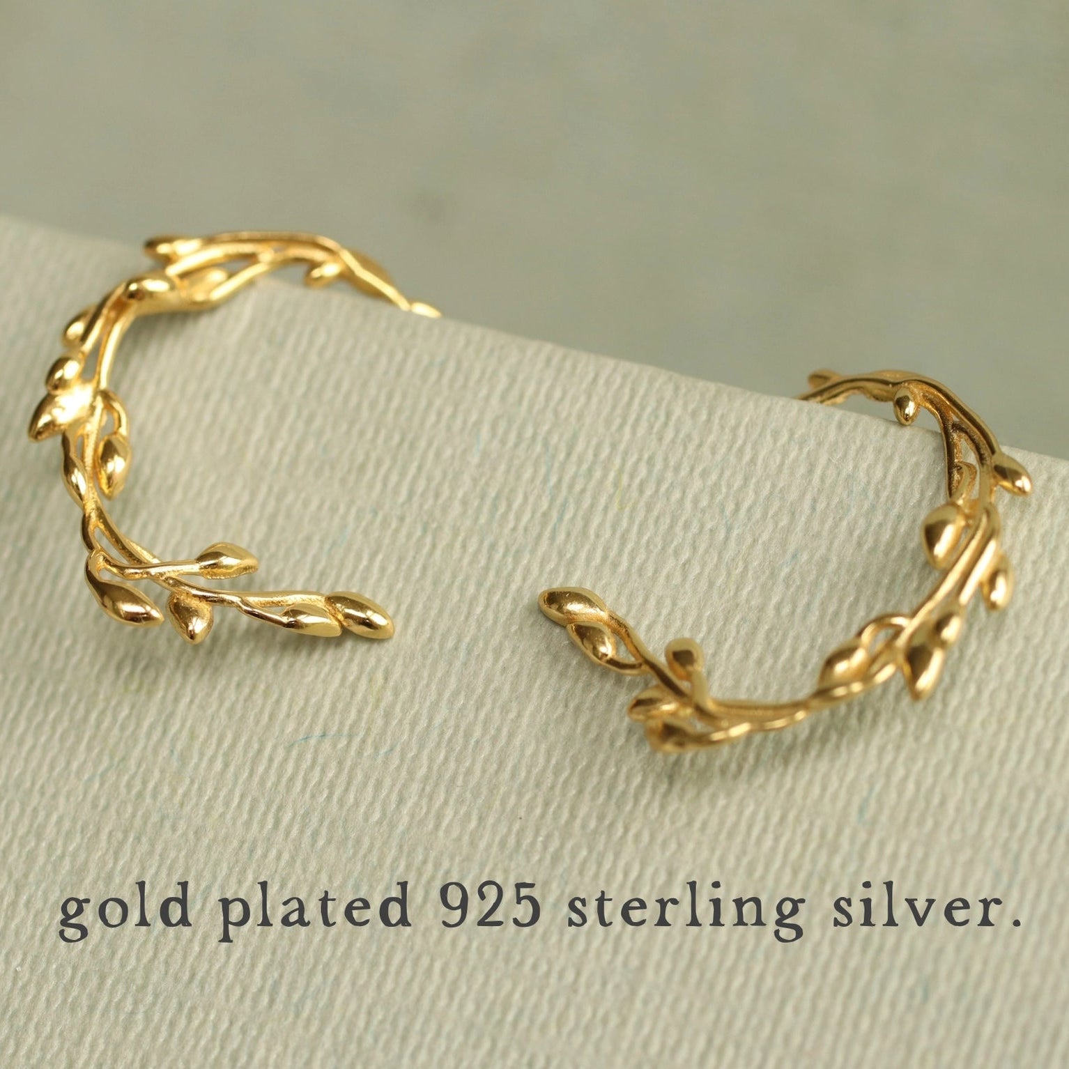 Close-up of the gold olive branch hoop earrings on a presentation card, highlighting their intricate details.
