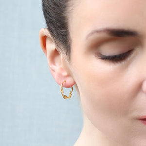 A close-up side profile of a woman wearing the gold-plated olive branch hoop earrings.