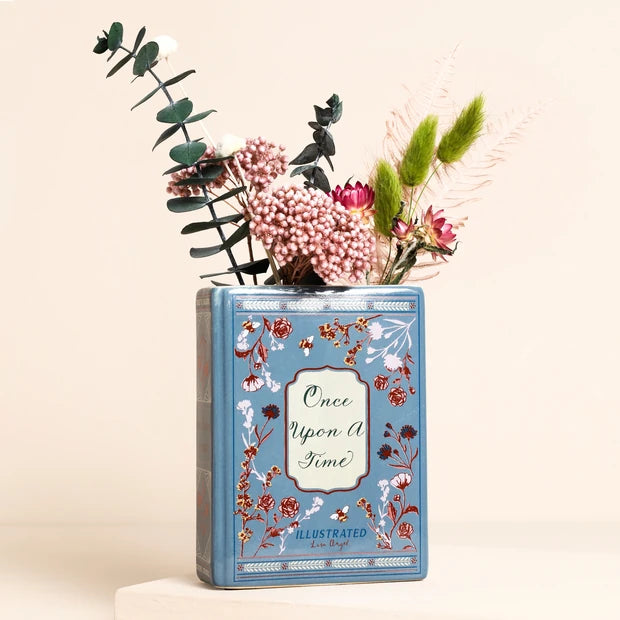 Mini ceramic book-shaped vase with “Once Upon A Time” design holding dried flowers.