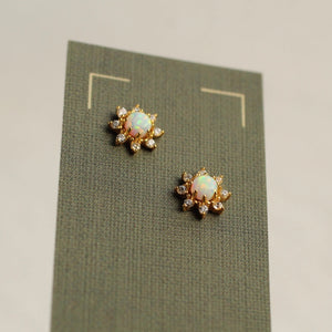 Pair of opal flower stud earrings displayed on textured green presentation card, highlighting the gold-plated setting and iridescent opals.