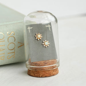 Gold opal flower earrings showcased inside a glass dome with cork base, styled beside a mint green book with gold foil lettering.