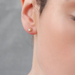 Close-up of opal flower stud earring worn in ear, showing the glowing white opal and gold-plated floral design against natural skin tone.