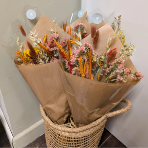 A rustic orange dried flower arrangement wrapped in kraft paper, placed in a woven basket.