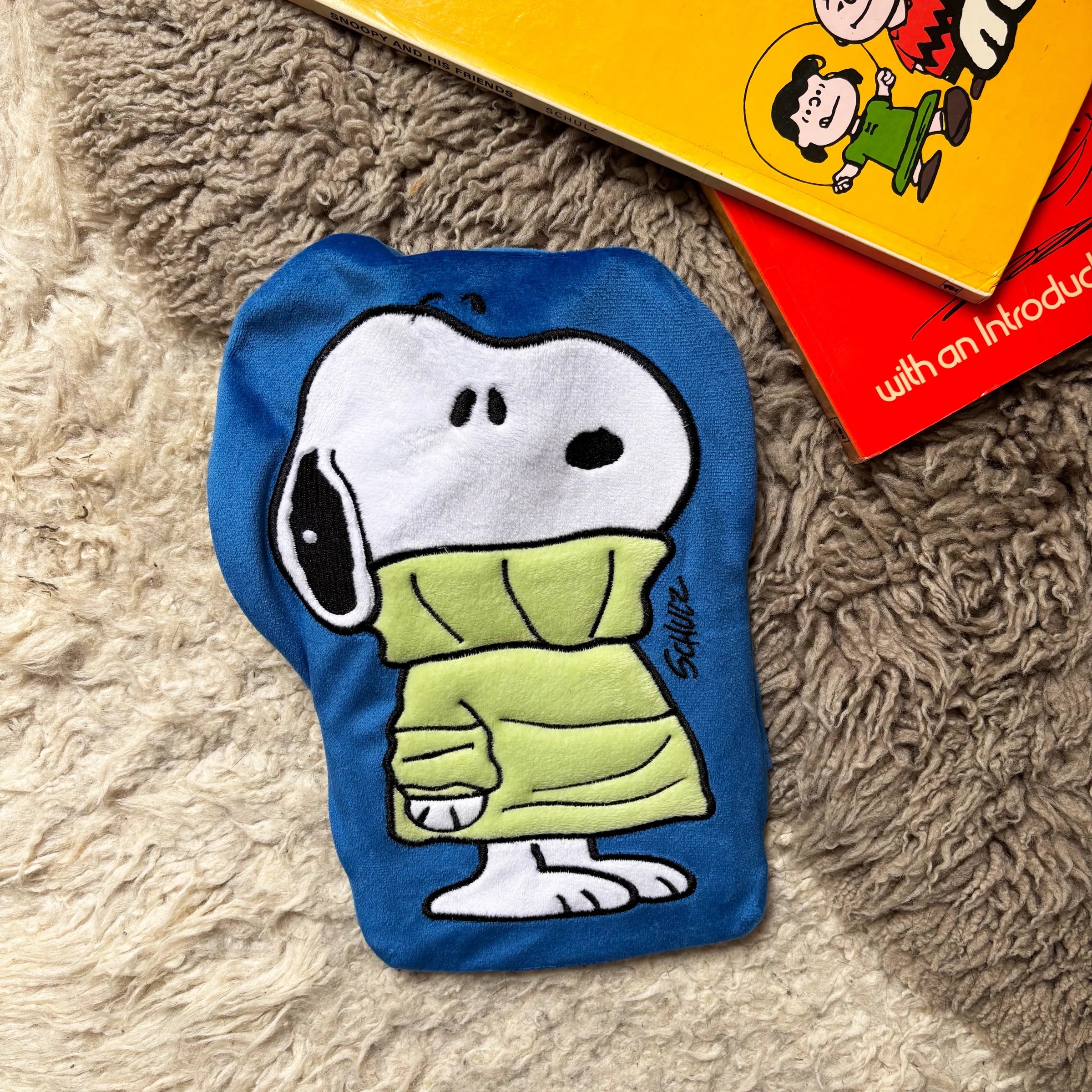 Peanuts Snoopy Jumper mini hot water bottle on rug with books.