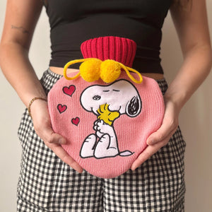 Woman holding Peanuts Snoopy Love Hot Water Bottle with yellow pompoms and heart design.