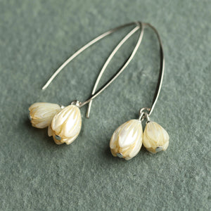 Angled shot of pearl snowdrop earrings showing iridescent mother of pearl petals and long silver hooks against a textured green backdrop.