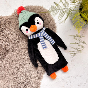 Penguin Hot Water Bottle with knitted hat and scarf lying on soft rug.