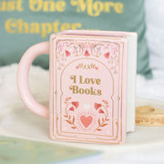 Pink ceramic book shaped mug with “I Love Books” text and floral design, styled on a tray.