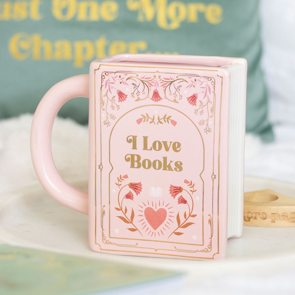 Pink ceramic book shaped mug with “I Love Books” text and floral design, styled on a tray.