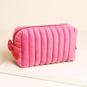 Pink velvet makeup bag with red bow and zip on cream background.