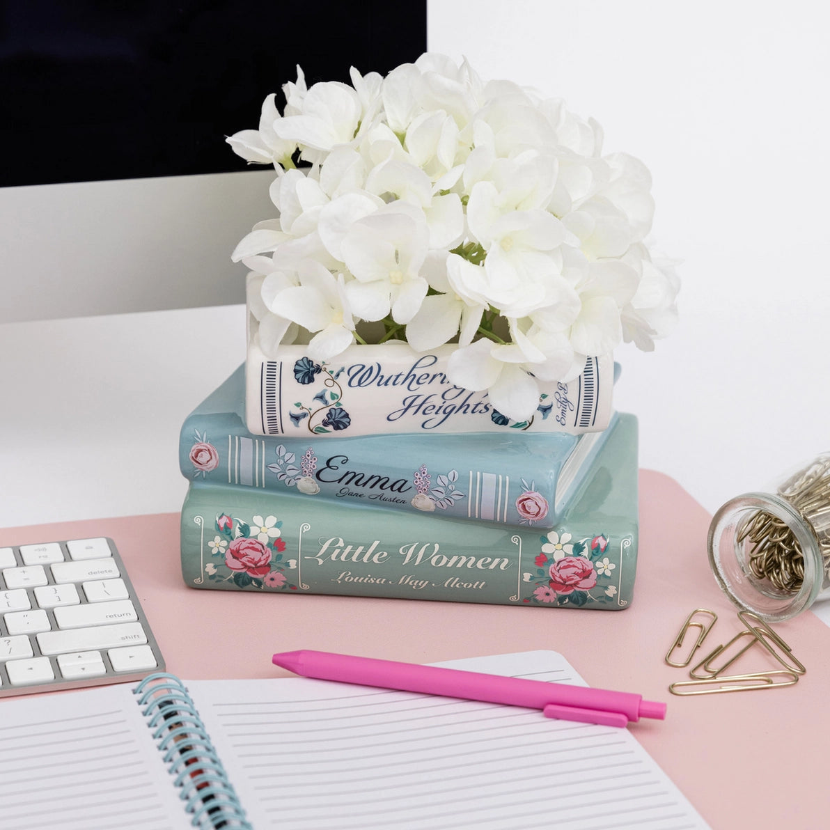 Stacked books ceramic planter styled on desk with white flowers.