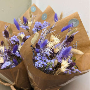 A beautifully wrapped purple dried flower arrangement displayed in a woven basket.