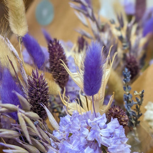 A close-up of delicate dried flowers and grasses in purple, cream, and neutral tones.