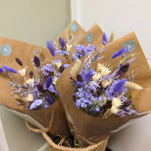 Multiple bouquets of purple dried flowers wrapped in kraft paper in a natural setting.