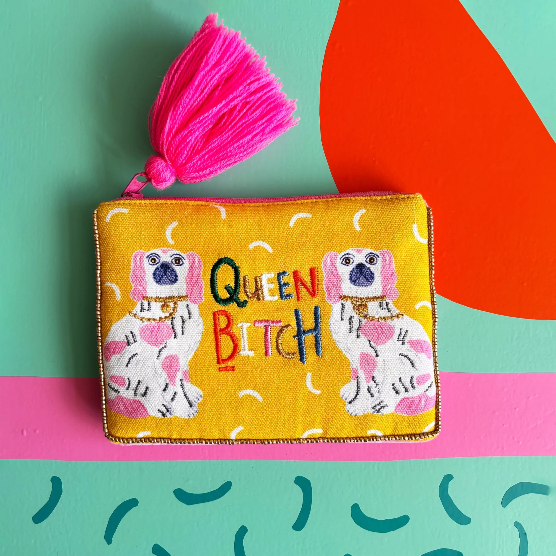 Flat lay of yellow pouch featuring embroidered slogan and dogs.