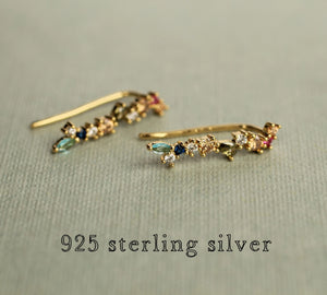 Pair of rainbow gemstone earrings lying flat on pale green fabric, showcasing 925 sterling silver gold-plated hooks and colourful cubic zirconia stones.