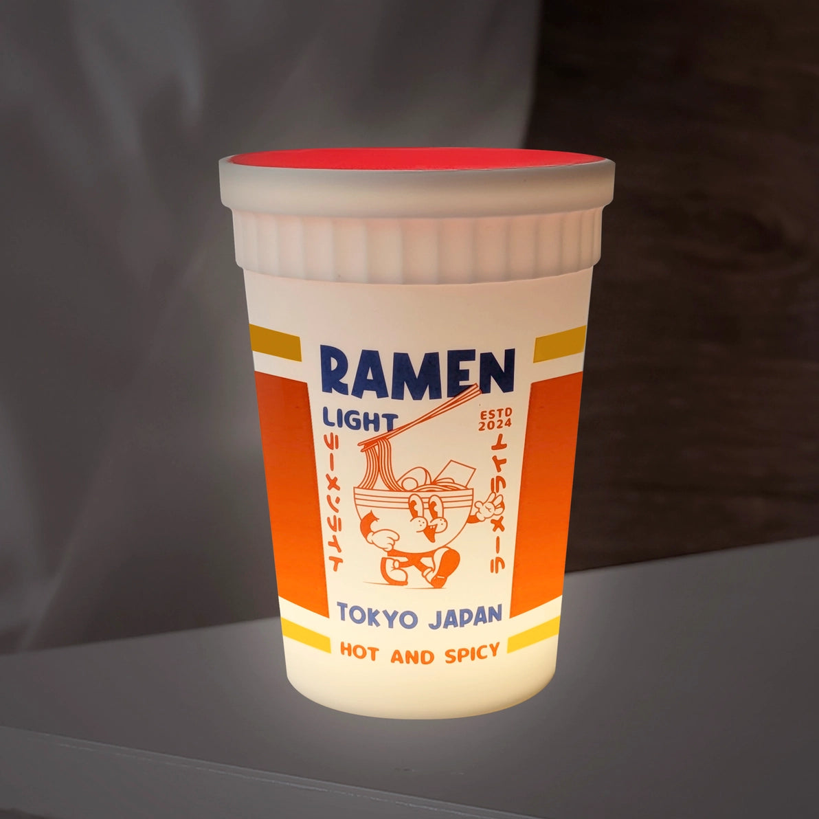 Side profile of the glowing Ramen Light lamp showing its red lid and vibrant orange panel design.