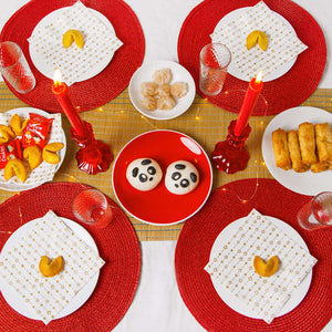 Pair of red glass candle holders styled on a table with fortune cookies, bamboo placemats, and dumplings for a colourful dinner setting.
