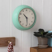 Mint-green retro wall clock on white wood panelling with shelf and plant