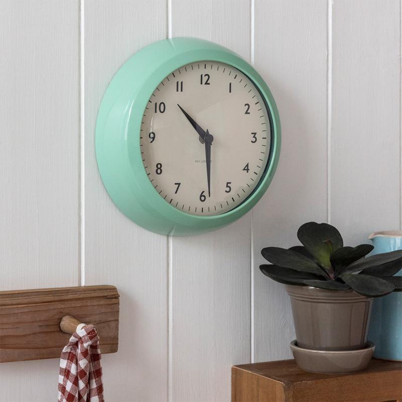 Mint-green retro wall clock on white wood panelling with shelf and plant