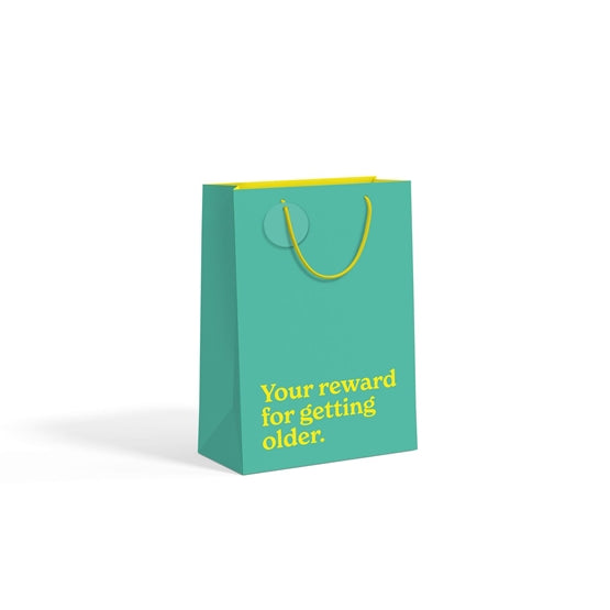 Teal medium gift bag with gold slogan text on white background.
