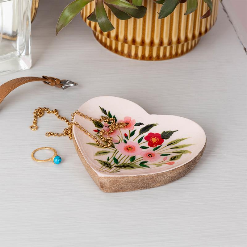 Front view of heart-shaped wooden trinket dish with floral design, placed on a dresser with gold jewellery.