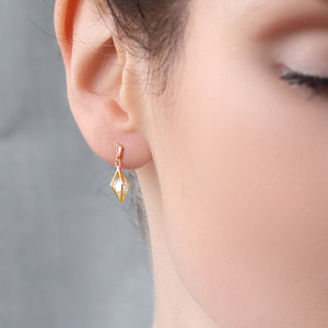 Model wearing gold rhombus geometric earring with crystal stone, shown just below the earlobe.