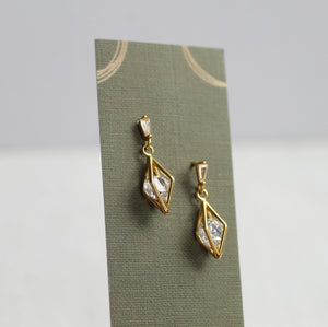 Side view of geometric gold and crystal earrings displayed on a green card.