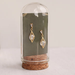 Pair of rhombus drop earrings displayed upright in a glass dome with cork base.