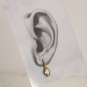 One gold crystal earring placed against a monochrome ear illustration for visual fit.
