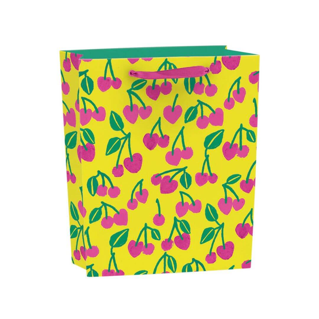 Medium recyclable gift bag with pink cherry illustrations and green leaves on a vibrant yellow background, finished with pink grosgrain ribbon handles and matching gift tag.