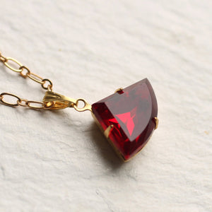 Close-up of the Ruby Deco Necklace with a faceted ruby-red vintage glass stone set in gold.