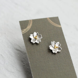 Silver Sakura flower stud earrings with gold centres mounted on a patterned display card – dainty sterling silver gift earrings.