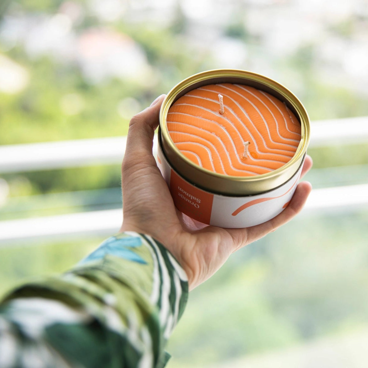 Person holding the Orange Salmon CandleCan outdoors, showcasing the tin’s opened lid and detailed wax surface resembling raw salmon.