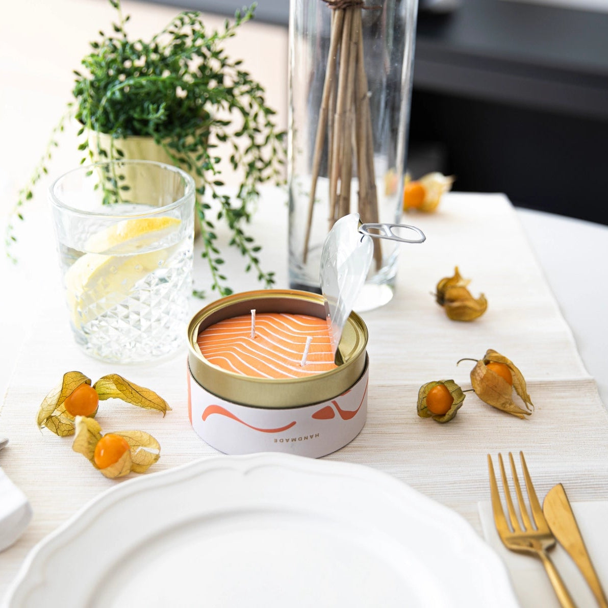 Orange Salmon tin candle displayed on a dining table with gold cutlery, physalis fruit, and elegant table setting.