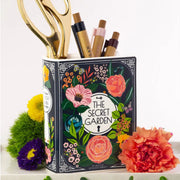 Secret Garden book vase used as a pen and scissor holder on a desk with flowers and props