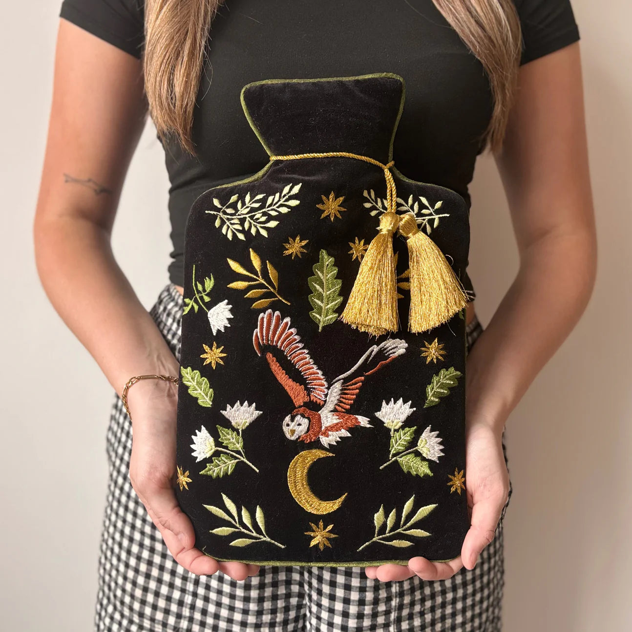 Woman holding embroidered owl velvet hot water bottle with tassel.