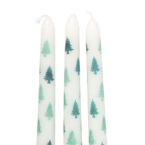 Close-up of Christmas tree design on white taper candles showing forest pattern in detail.