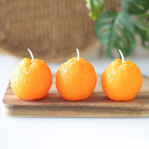Front view of 3 orange-shaped novelty candles on a wooden tray.