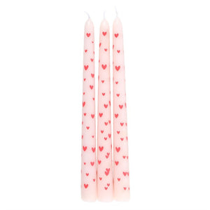 Three pink taper candles decorated with red hearts, standing upright on white background, ideal for romantic table settings or home décor.
